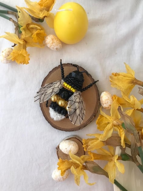 A close-up shot of a bumblebee landing on the edge of a shallow dish filled with water and small stones. The stones provide a safe landing spot for the bee to drink without the risk of drowning, demonstrating an easy way to create a bee-friendly water source.
