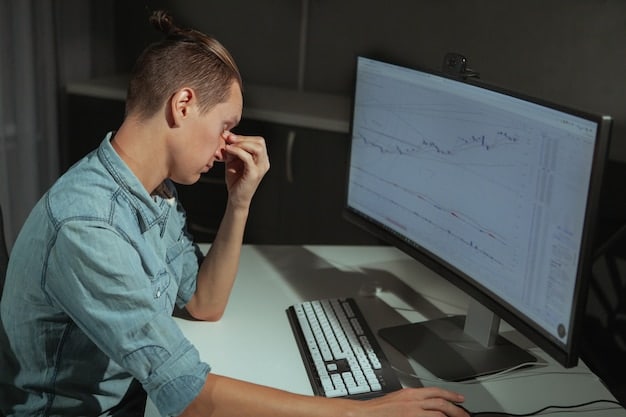 A stressed person sitting at a desk with their head in their hands while looking at a computer screen with charts decreasing, signifying negative financial strain.