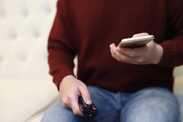 A person holding a remote control in one hand and a smartphone in the other, signifying the viewer's ability to choose between traditional TV and streaming services. The room is partially dark, emphasizing the immersive experience of watching TV.