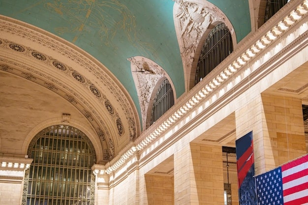 A close-up of the Federal Reserve building in Washington D.C., with a blurred background of people walking by. The image conveys a sense of institutional power and economic influence. The focus is on the building's architecture and the American flag waving in the background.