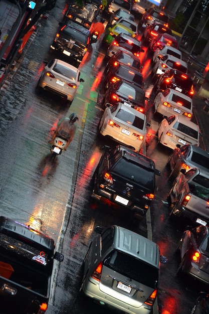 A high-angle shot of cars gridlocked on a busy highway during rush hour in a major US city. Brake lights are illuminated, adding a red glow to the scene. Skyscrapers are visible in the background, partially obscured by smog. This illustrates the daily commute for many Americans and relates directly to why Mind-Blowing: The Average American Drives Over 13,000 Miles Per Year.