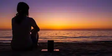 Digital Detox: 2 Effective Strategies Americans Are Using to Disconnect and Recharge Their Minds This Year Person on beach at sunset, smartphone face down, symbolizing digital detox and mental recharge.